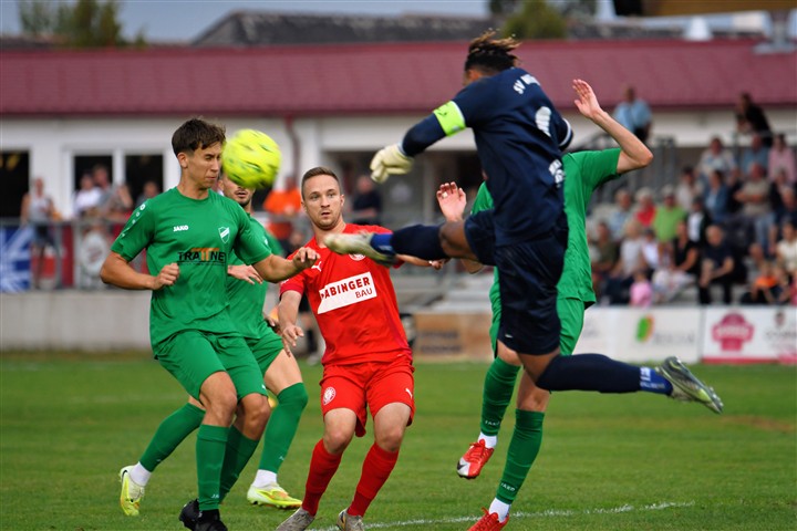 Fußball: Torhüter im Sprung, Spieler in Rot und Grün im Zweikampf um den Ball