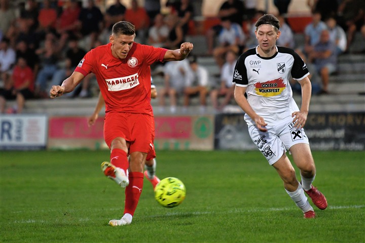 Fußballer in Rot schießt auf Tor, Spieler in Weiß verteidigt, bei einem Spiel in Österreich